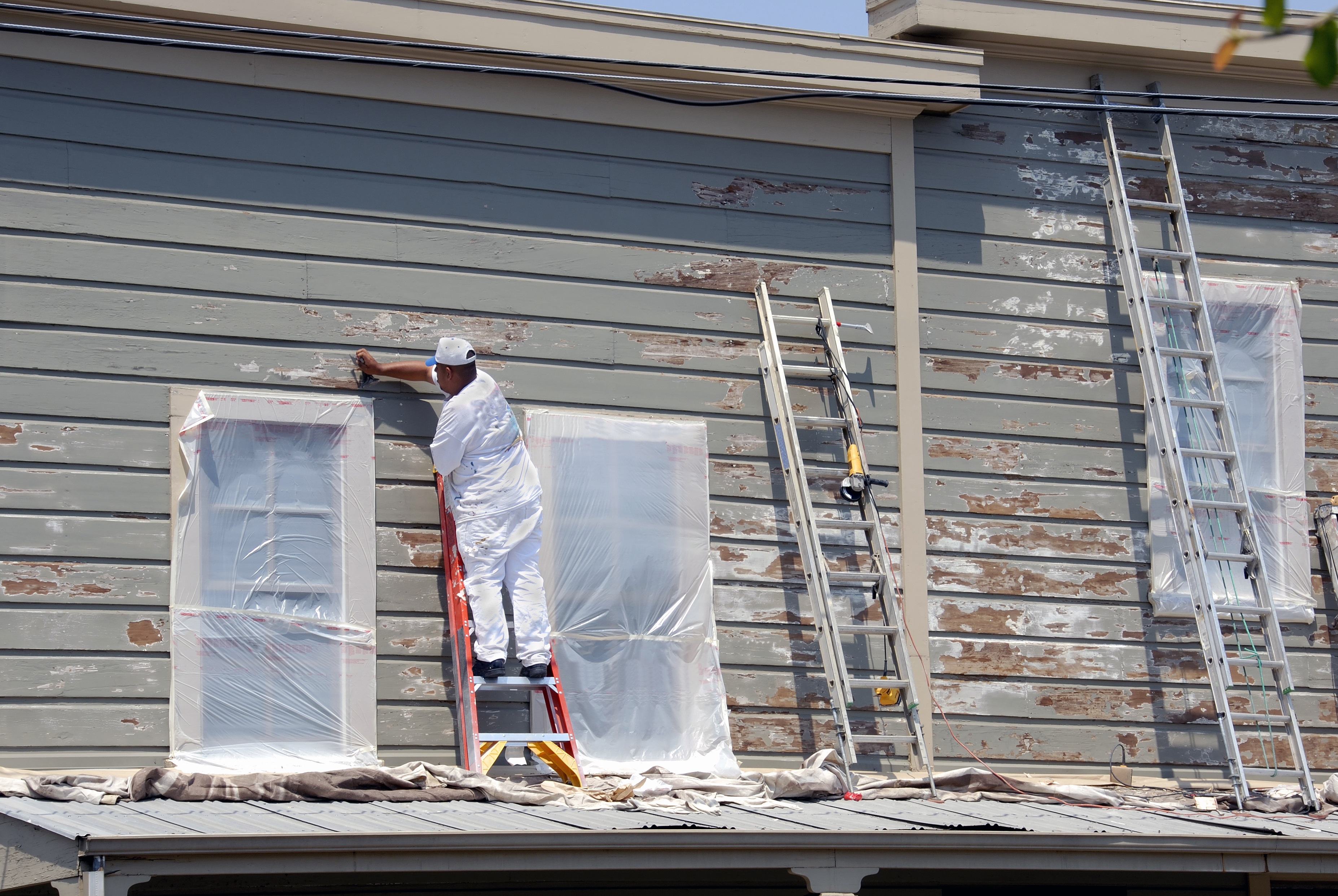 Painter scraping paint from house