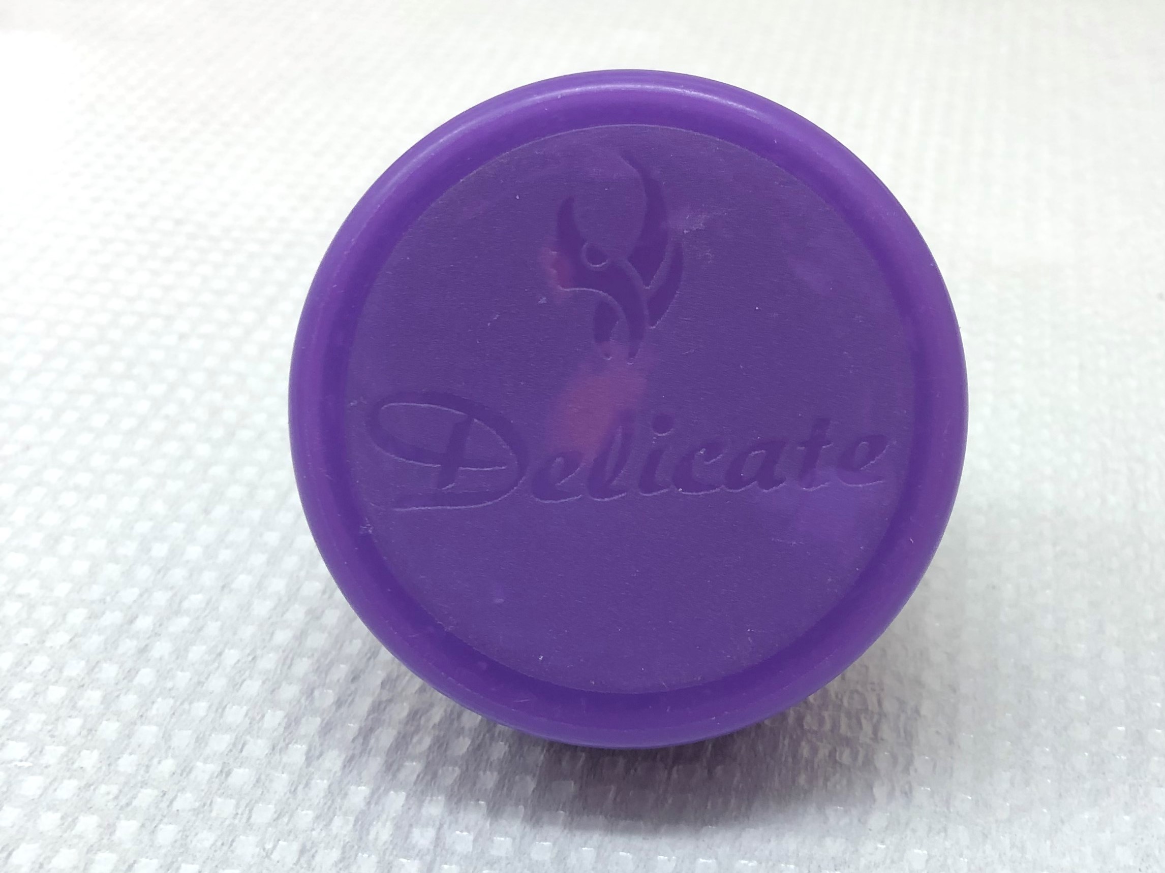 small round purple container of face cream with the word "delicate" inscribed in the cap