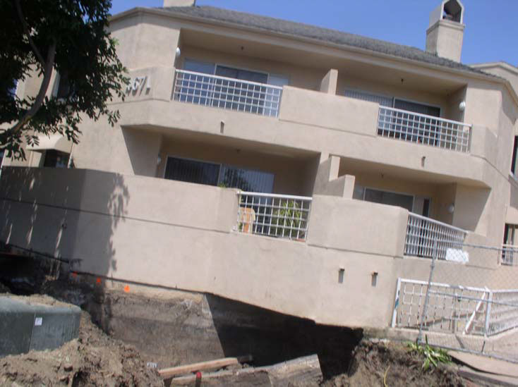 The apartment terraces overhang a deep dirt pit that extends beneath the street level of the building.