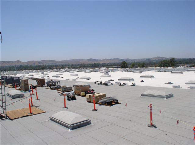 A large, flat, white building rooftop stretches into the horizon and is covered with scores of skylights. There are mountains in the distance.