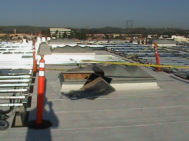 Yellow incident scene tape blocks off a broken skylight with two flexible black solar panels placed against it. There are metal rods on the surrounding rooftop where solar planels are meant to be placed.