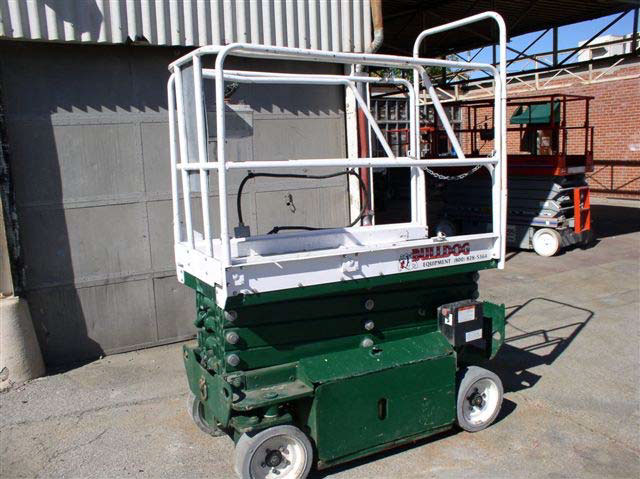 A green and white scissor lift with wheels. The top basket portion is white and the bottom lift section is green.