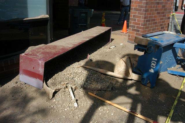 A dark red and wide planter box lies on its side on a concrete sidewalk with rocks and soil spilled over a wide area.