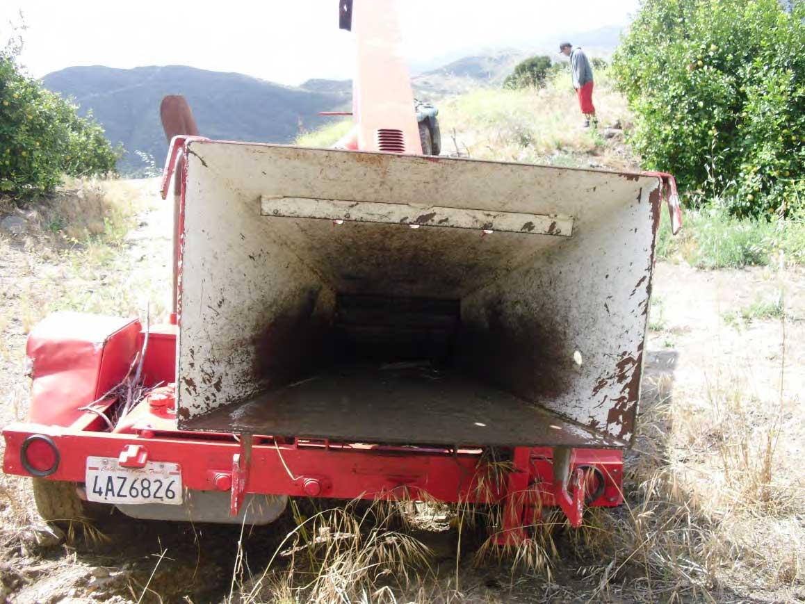 A straight-on view of the back of the chipper. A license plate is on the lower left side and the opening to the in-feed hopper is positioned to the right and above the frame of the trailer.