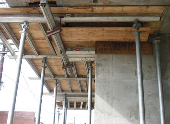 The vertical shoring is shown from beneath with poles supporting plywood boards.