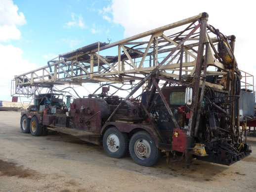 Photo showing mobile oil well servicing rig, which is a very large, old truck with many heavy metal moving parts.