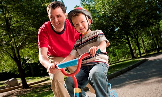 Father helping young son ride a bike outside