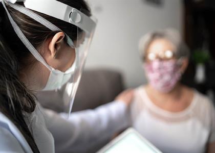 This photo shows a nurse with PPE talking with a person wearing a mask